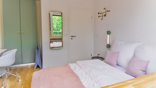 Une chambre à coucher comprenant un lit, un bureau, une chaise, une armoire et un miroir.