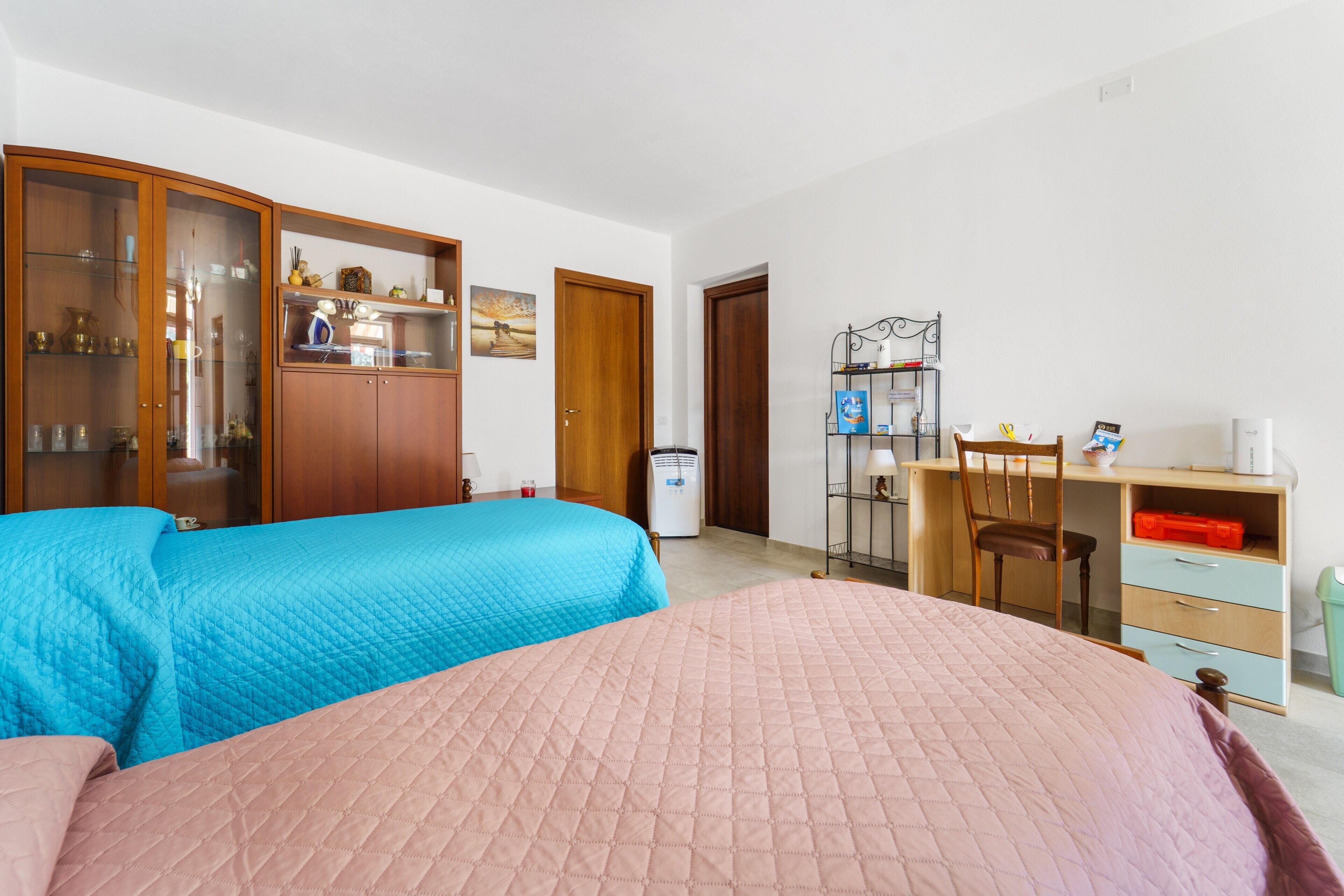 Un dormitorio con dos camas, un armario de madera, un escritorio con silla y una pequeña estantería.