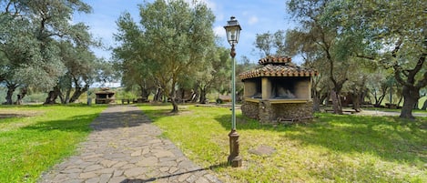 A stone pathway leading to a gazebo-like structure with a lamp post, surrounded by trees.