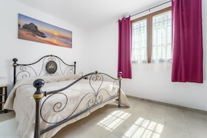 A bedroom with a bed, a painting, a window with curtains, and a view of the outside.