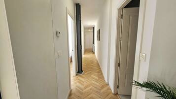 A hallway with a herringbone floor, white walls, and doors leading to rooms.