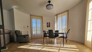 A spacious living room with a herringbone wood floor, a dining area with a table and chairs, and large windows with curtains. - Apartamentos Ciudadela Superior 3000 (Jaca)