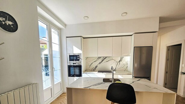 A modern kitchen with a marble countertop, stainless steel appliances, and a black bar stool. - Apartamentos Ciudadela Superior 3000 (Jaca)