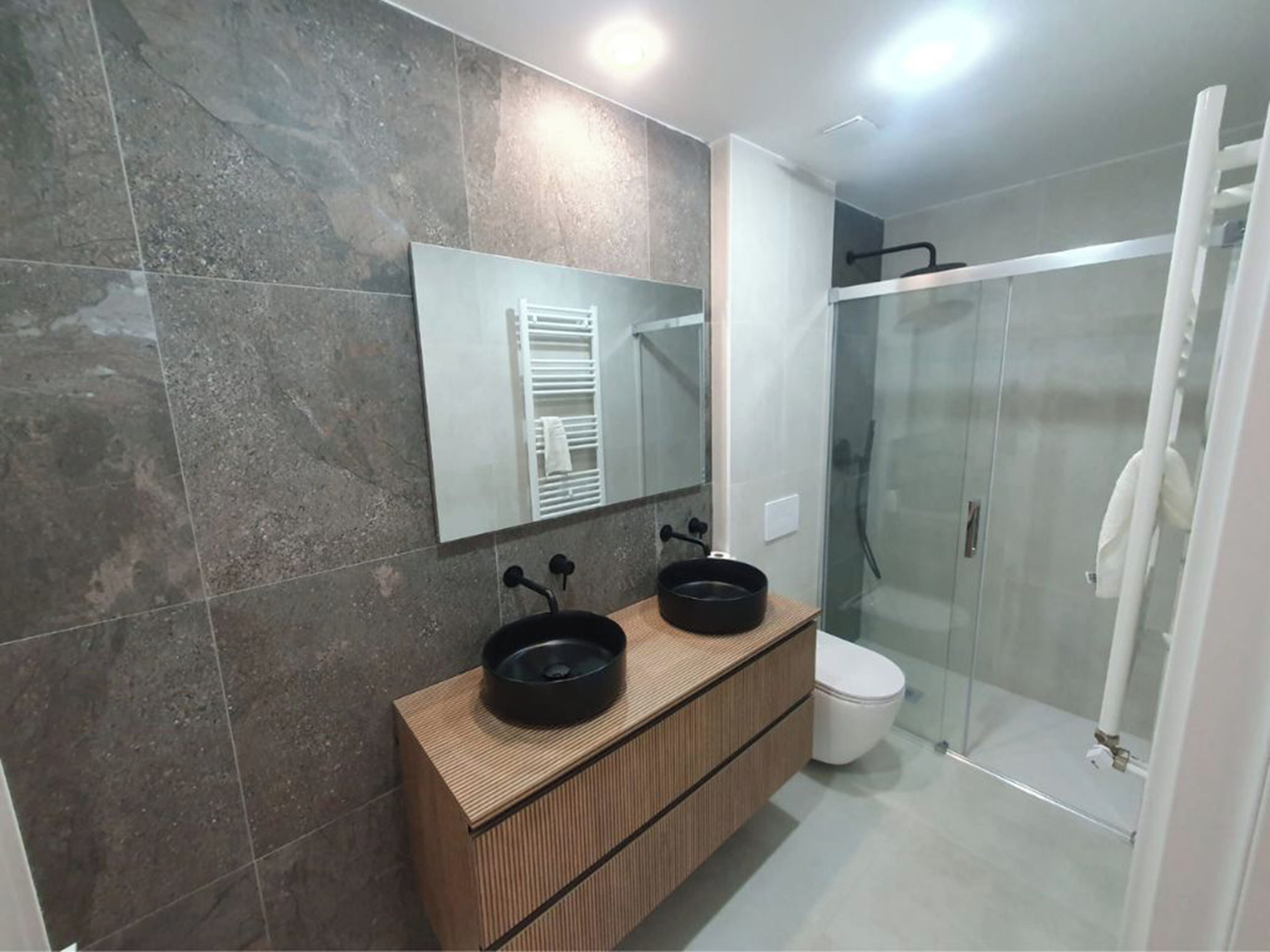 A modern bathroom with a wooden vanity, two black sinks, a glass shower enclosure, and a large mirror.