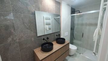 A modern bathroom with a wooden vanity, two black sinks, a glass shower enclosure, and a large mirror.