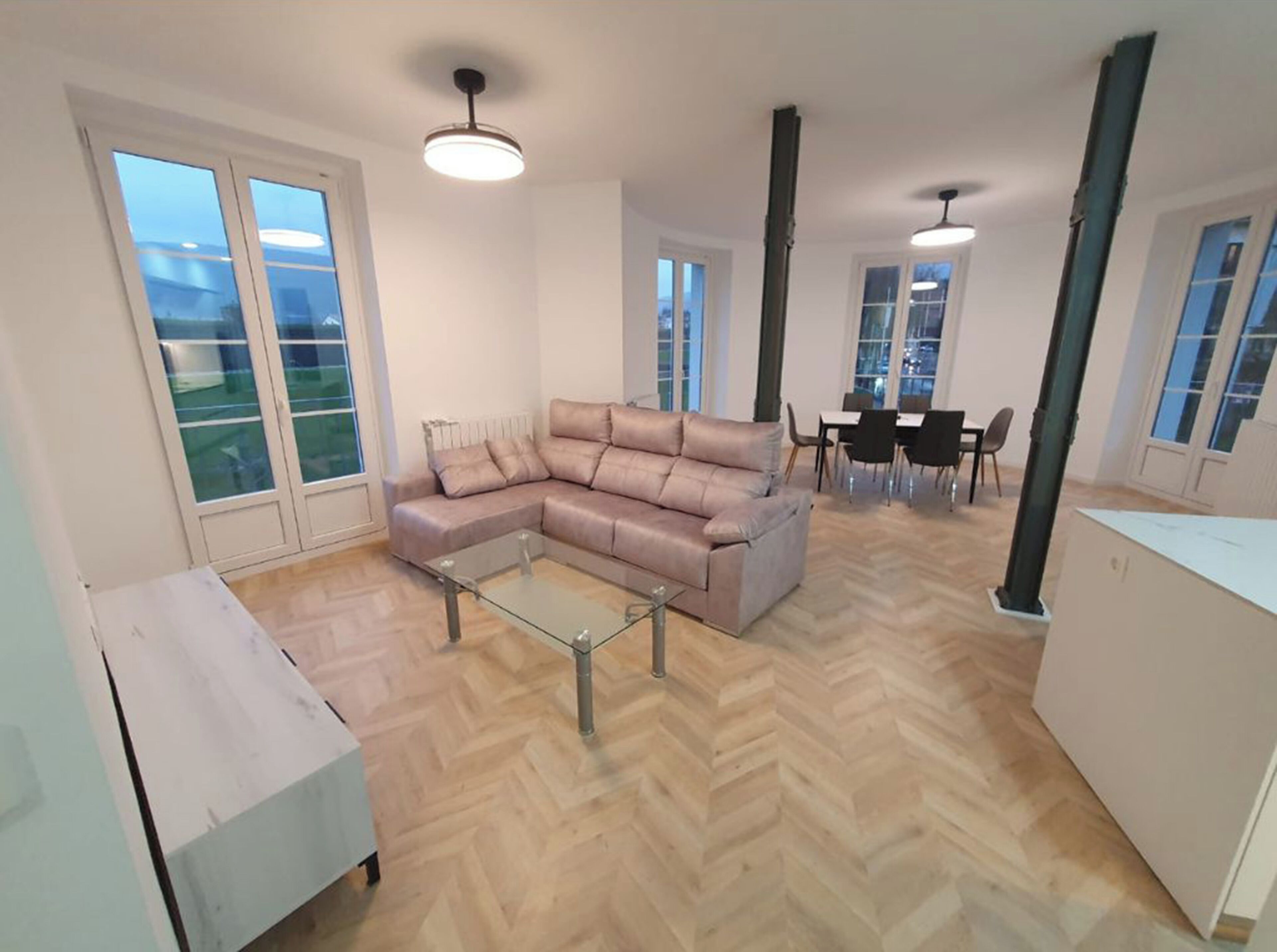 A modern living room with a sectional sofa, a glass coffee table, and a dining area with chairs and a table.