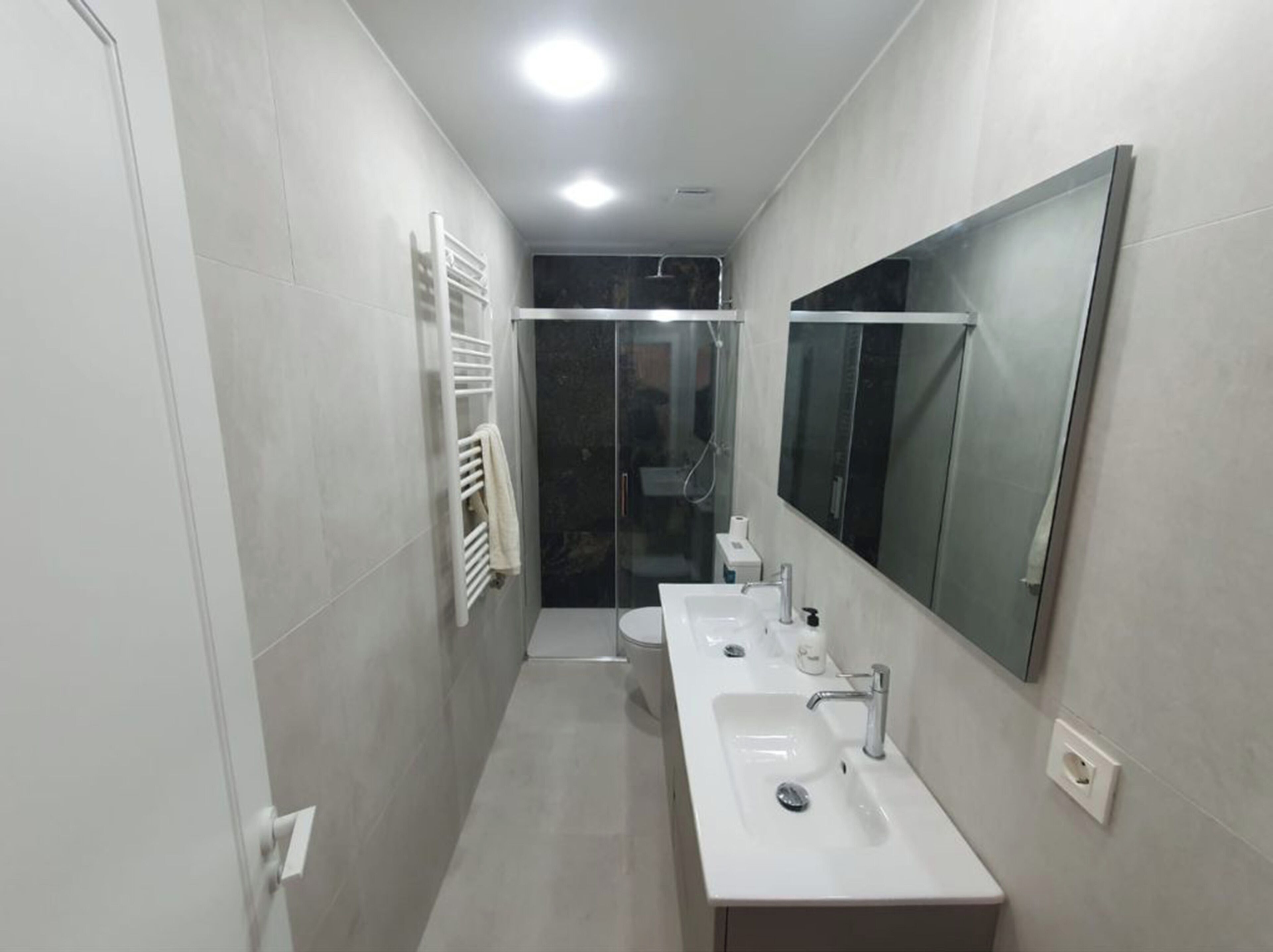 Et moderne badeværelse med to håndvaske, et stort spejl og en brusekabine i glas.