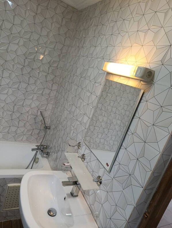 A bathroom with a geometric tile pattern on the walls, a white sink, and a mirror. - GUIM'S SQUARE HOTEL (Douala)