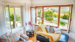 A cozy room with a sofa, a black couch, and a window with a view of greenery and buildings. - Moby Dick Lodge Colares (Sintra)