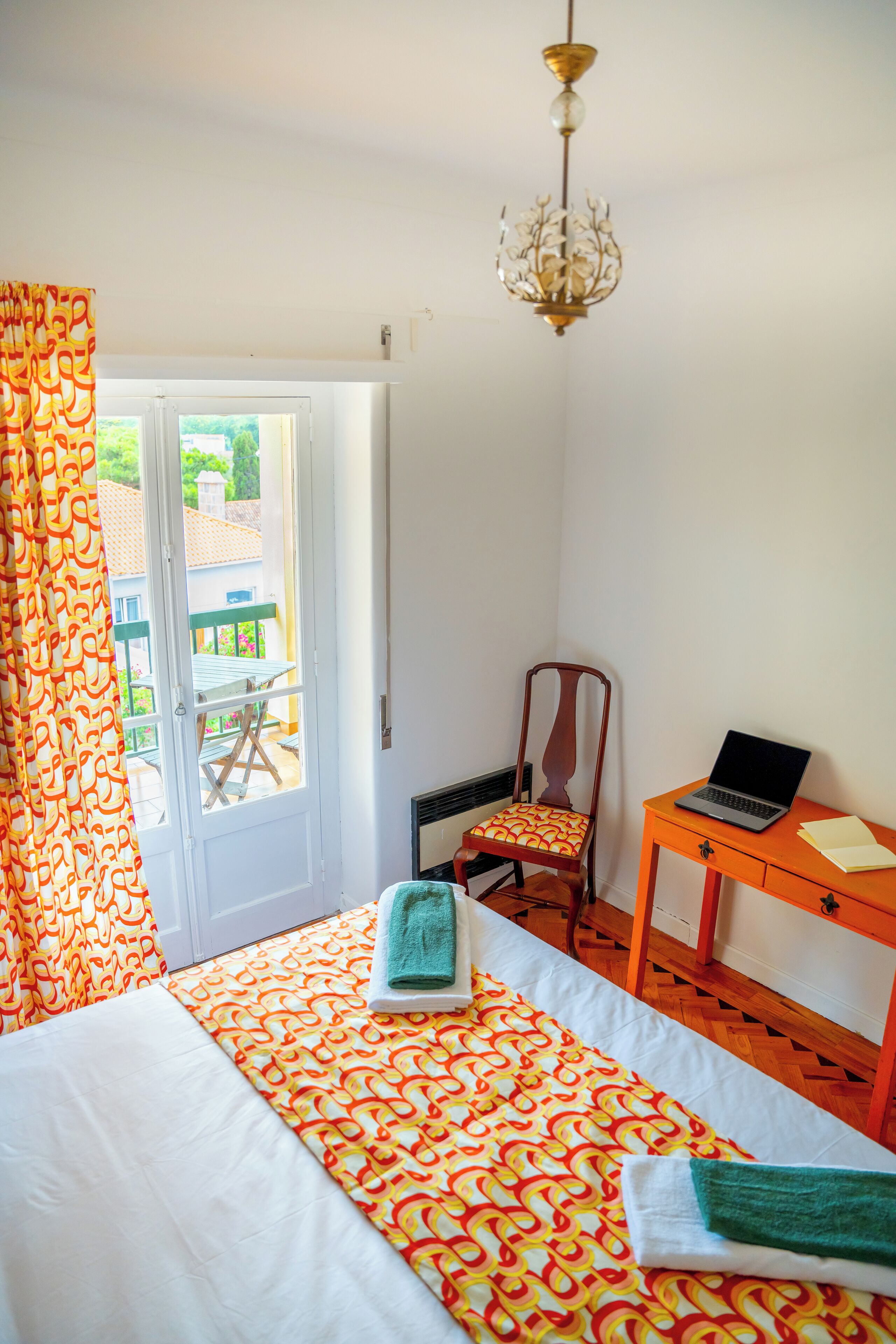 A bedroom with a bed, a chair, a desk with a laptop, and a window with curtains.