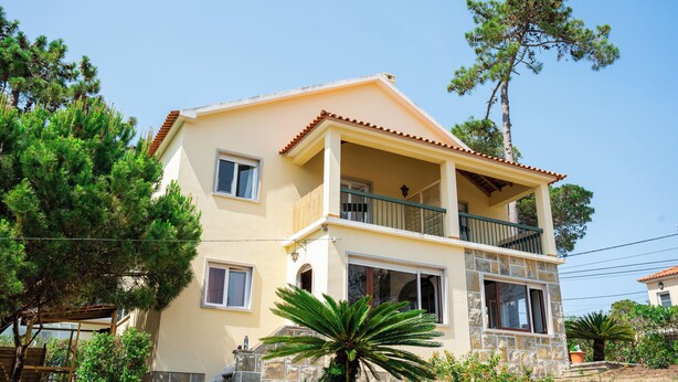 A two-story house with a balcony, surrounded by trees and a clear sky. - Moby Dick Lodge Colares (Sintra)