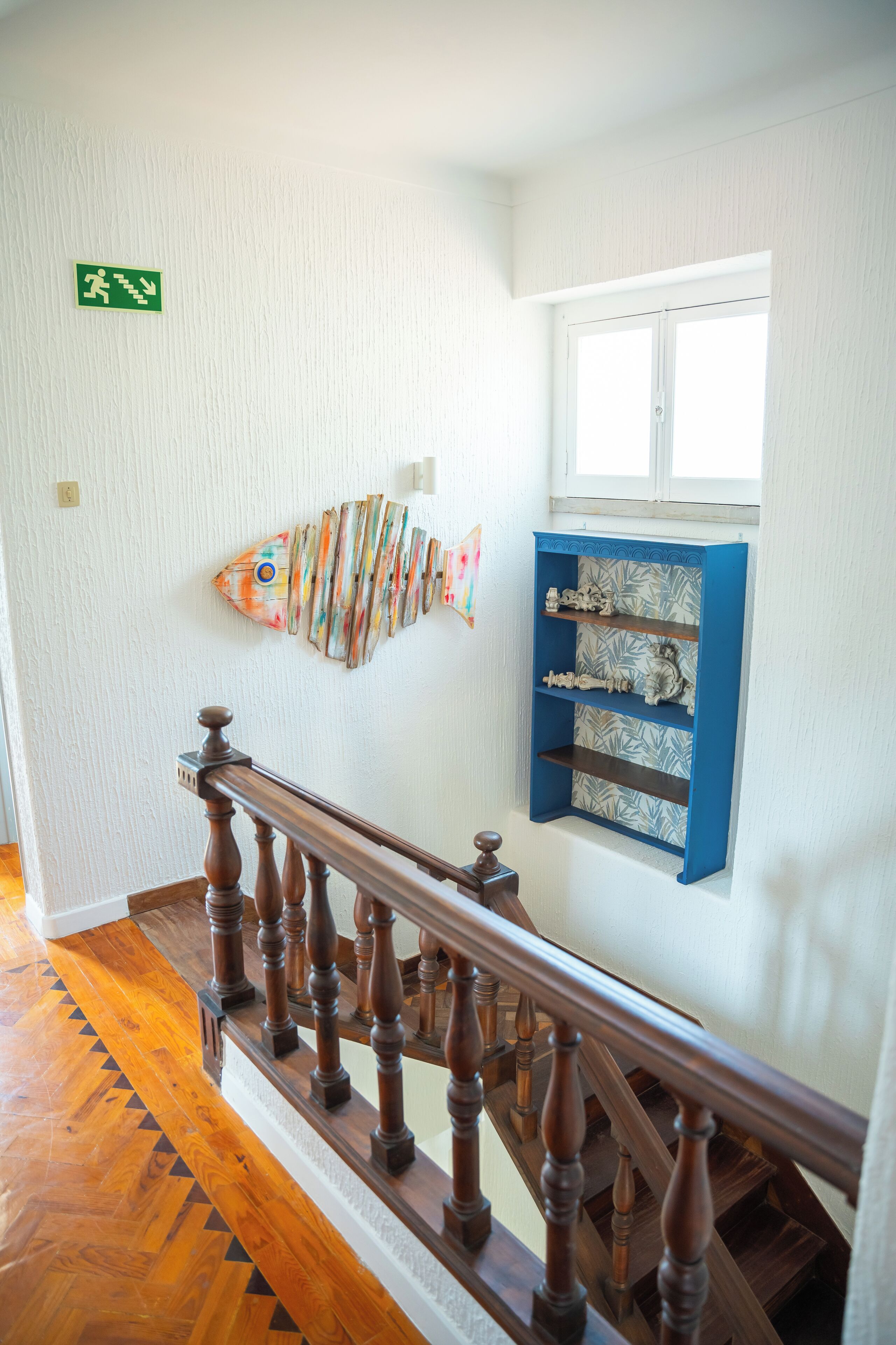 A staircase with wooden balusters, a wall-mounted fish decoration, and a blue shelf unit with patterned shelves.