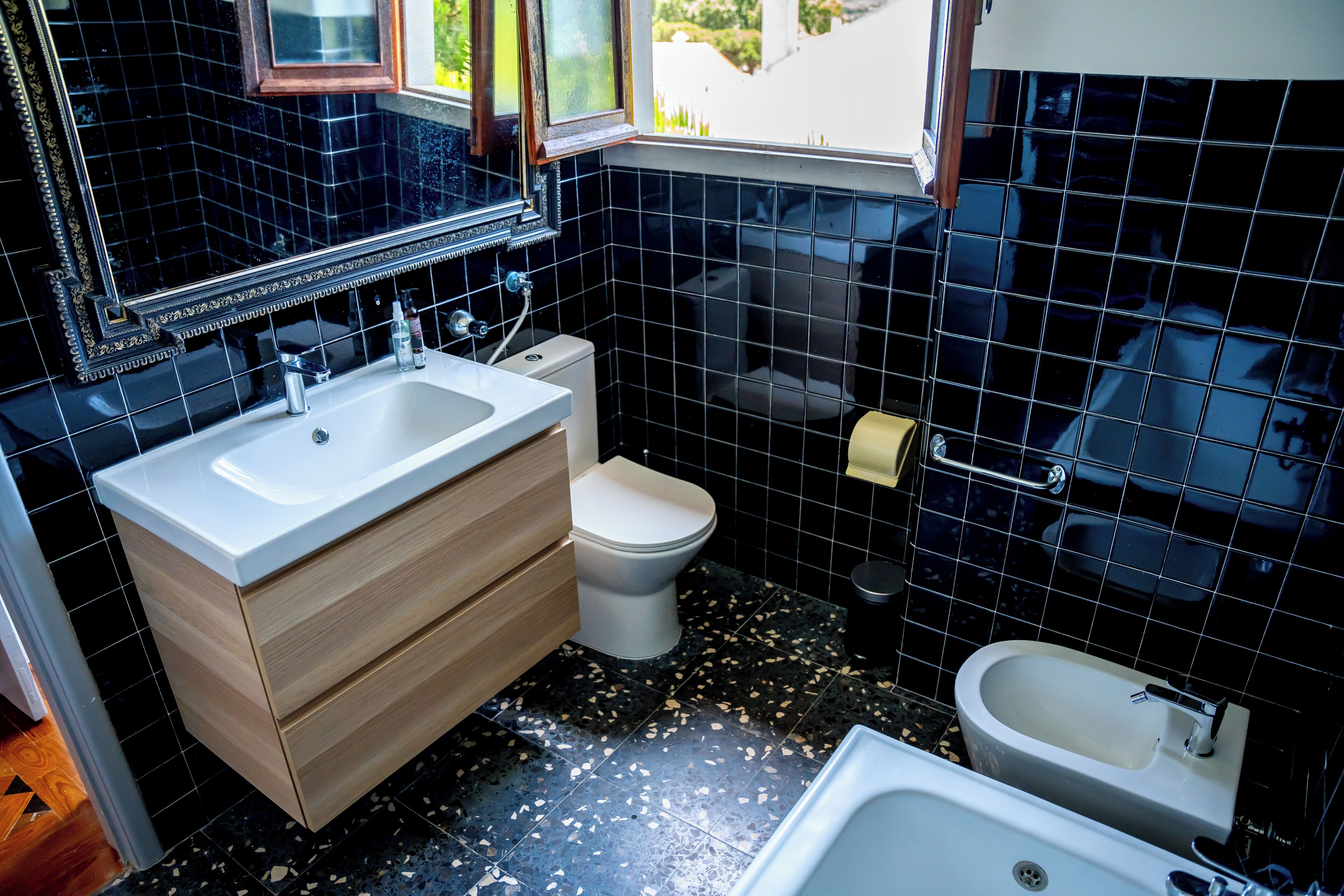A bathroom with black tiled walls, a white sink, a toilet, and a bathtub.