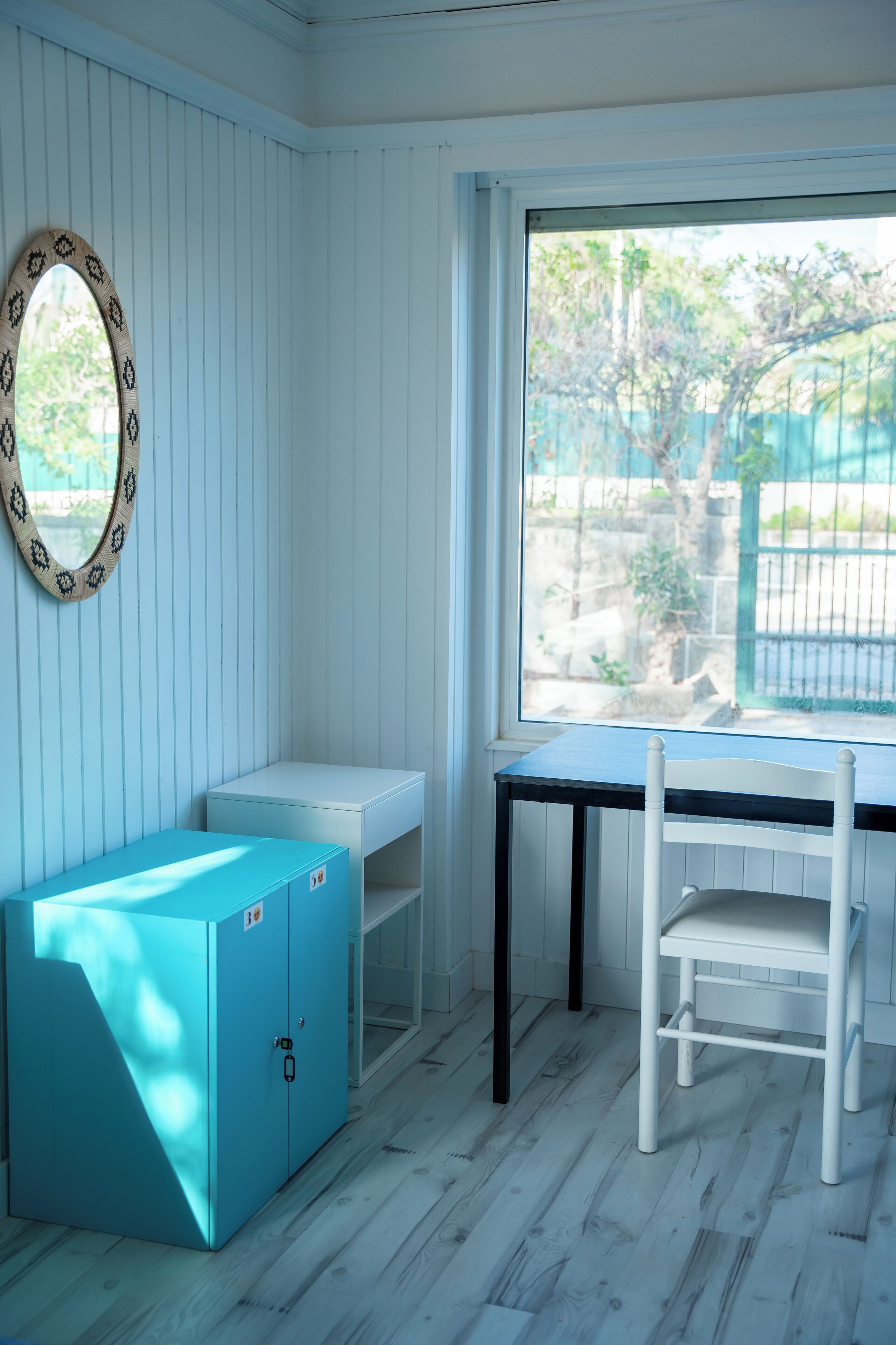 A room with a blue cabinet, a white chair, and a window with a view of greenery and a fence.