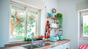 A kitchen with a sink, a washing machine, and a window with a view of trees. - Moby Dick Lodge Colares (Sintra)