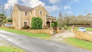 Une maison en pierre avec une allée pavée, un petit jardin et une voiture garée dans l’allée.