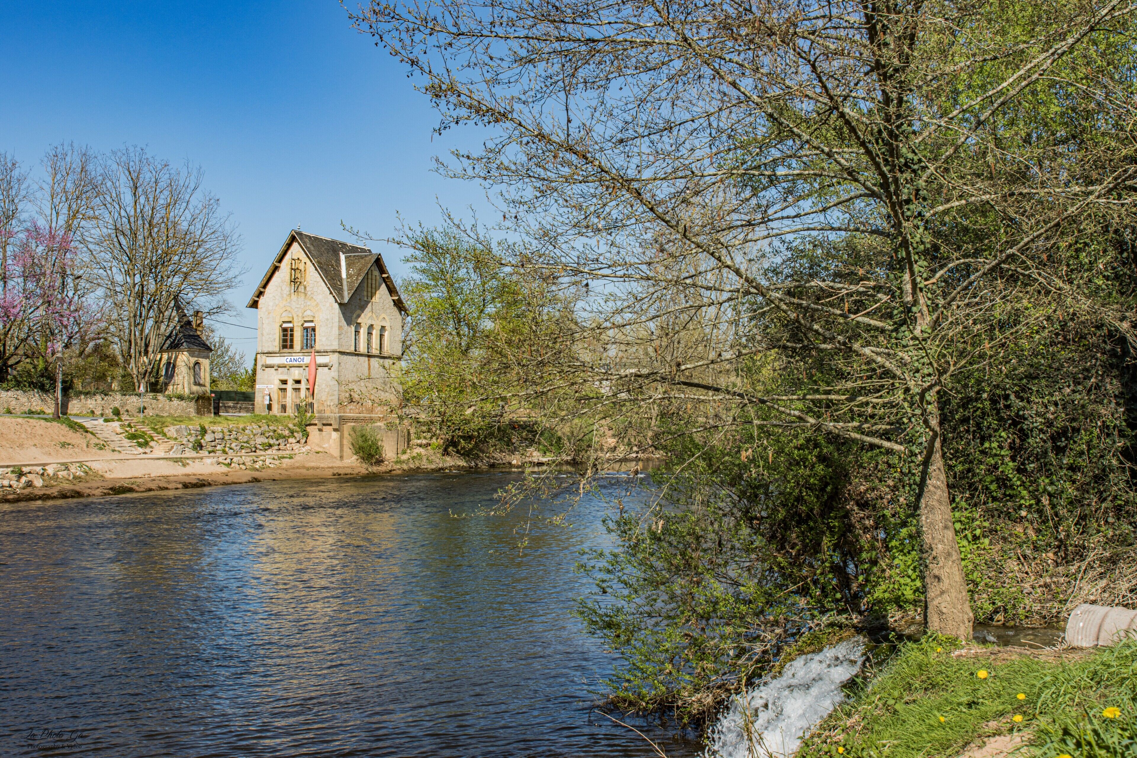 Ein Gebäude am Flussufer mit einem markanten Turm, einer Brücke und einer natürlichen Landschaft.