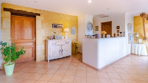 A reception area with a wooden door, stone wall, white reception desk, and a potted plant. - Bed and Breakfast 'Chambre Quietude' with Shared Terrace, Shared Garden and Wi-Fi (Saint-Amand de Coly)