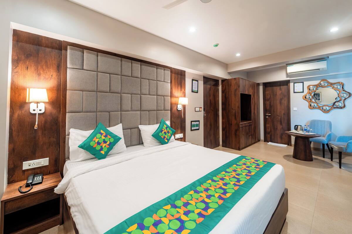 A hotel room with a large bed, wooden headboard, bedside lamps, a telephone, and a desk with a chair.