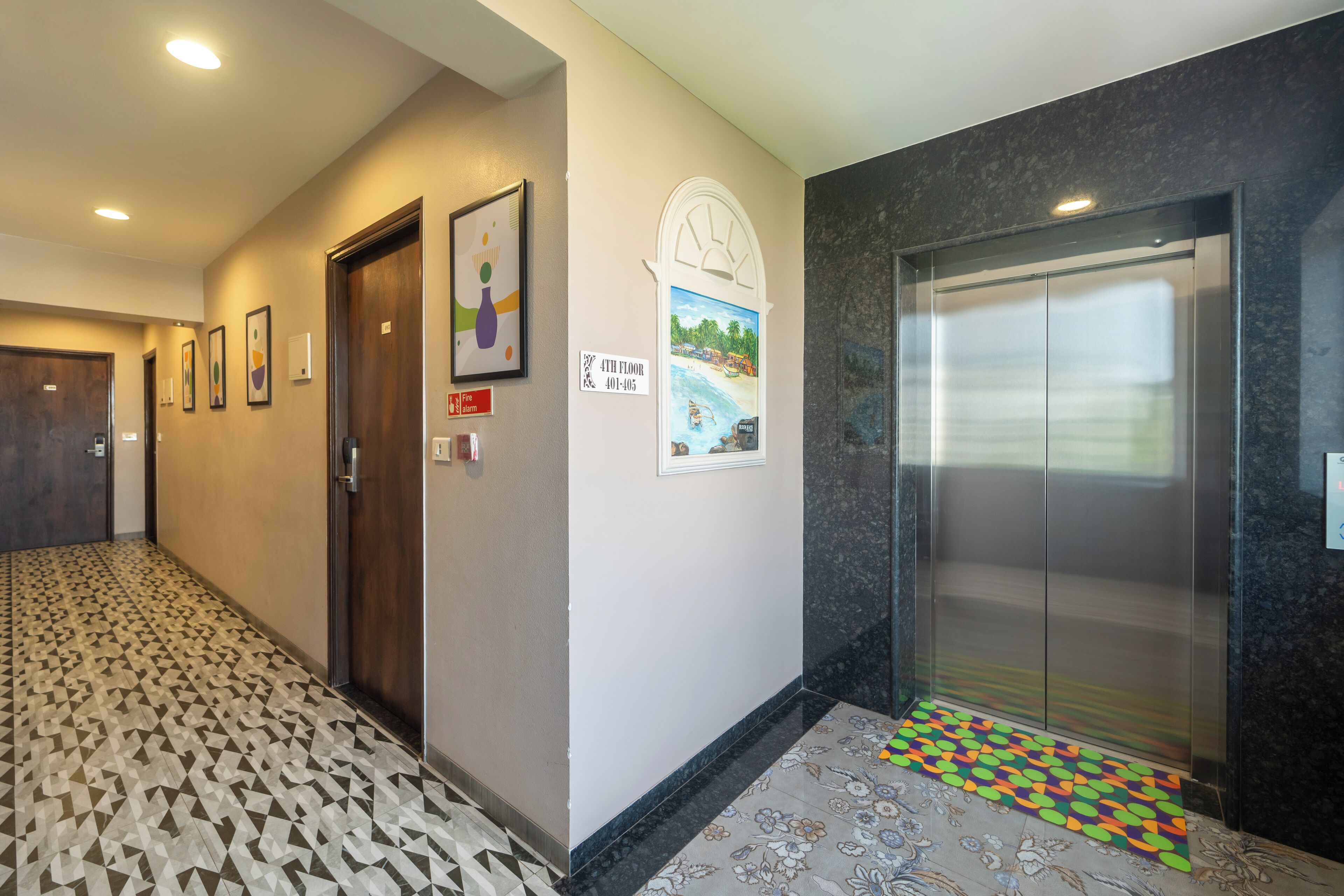 A hotel corridor with patterned flooring, a door, a wall-mounted sign, and an elevator.