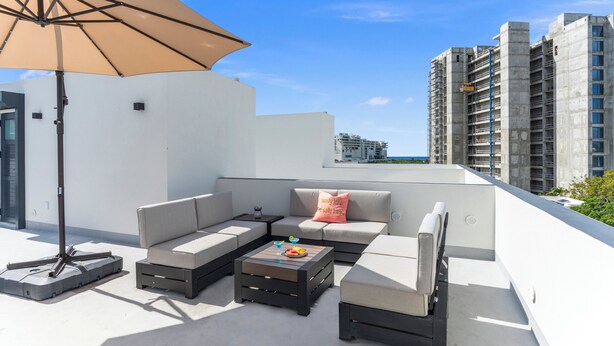 A rooftop terrace with a sectional sofa, a coffee table, and an umbrella. - Casa Bisani in Cupecoy (Sint Maarten)