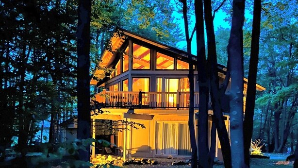 A two-story wooden cabin with a balcony, surrounded by trees. - Fabulous 3-bedroom chalet in Hidden Valley, PA; walk to the slopes! (Hidden Valley)