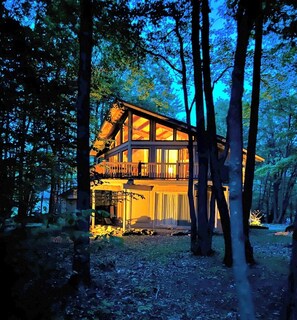 Une cabane en bois à deux étages, dotée d’un balcon et entourée d’arbres.