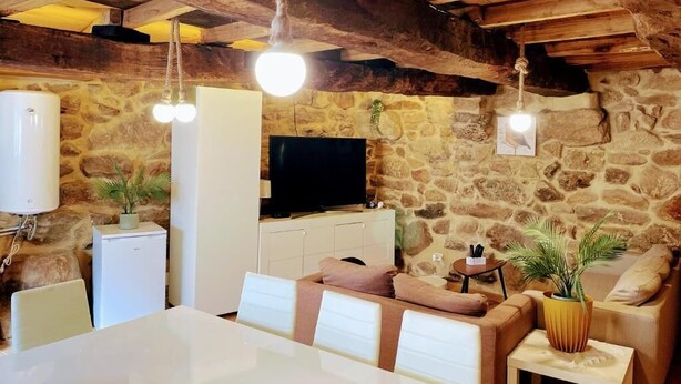 A rustic interior with exposed wooden beams, stone walls, a flat-screen TV, a dining table with chairs, and a sofa. - Charming Tourém Retreat 3 Bedroom House With Stunning Views (Montalegre)