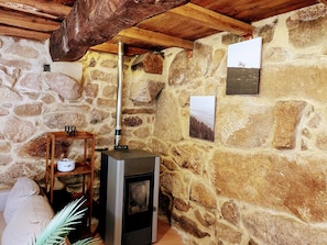 Ein Zimmer mit Steinwänden, einem Kaminofen, einem Regal mit einem Teekessel und gerahmten Bildern an der Wand.