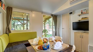 Quarto compacto com sofá, mesa de jantar posta para o café da manhã, televisão e janela com cortinas.