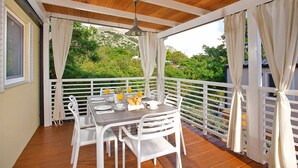 Uma área de refeições ao ar livre coberta, com teto de madeira, cadeiras brancas e mesa posta para o café da manhã.