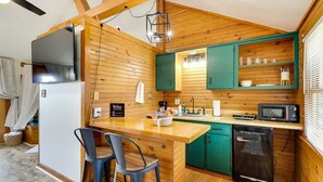 A compact kitchen with wooden walls, a central island with bar stools, a built-in microwave, and a dishwasher. - Hilltop Lookout #2 at Busch Mt- Stunning Views! (Eureka Springs)