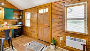 A compact kitchen with wooden walls, a central door, and a window with blinds. - Hilltop Lookout #2 at Busch Mt- Stunning Views! (Eureka Springs)