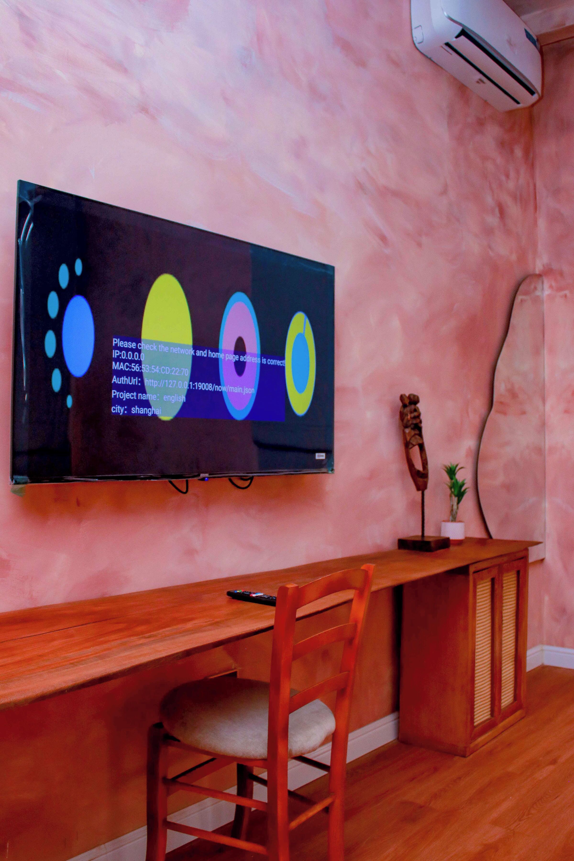 Une pièce comprenant un bureau en bois, une chaise, un téléviseur fixé au mur qui affiche du texte, et un objet décoratif posé sur le bureau.