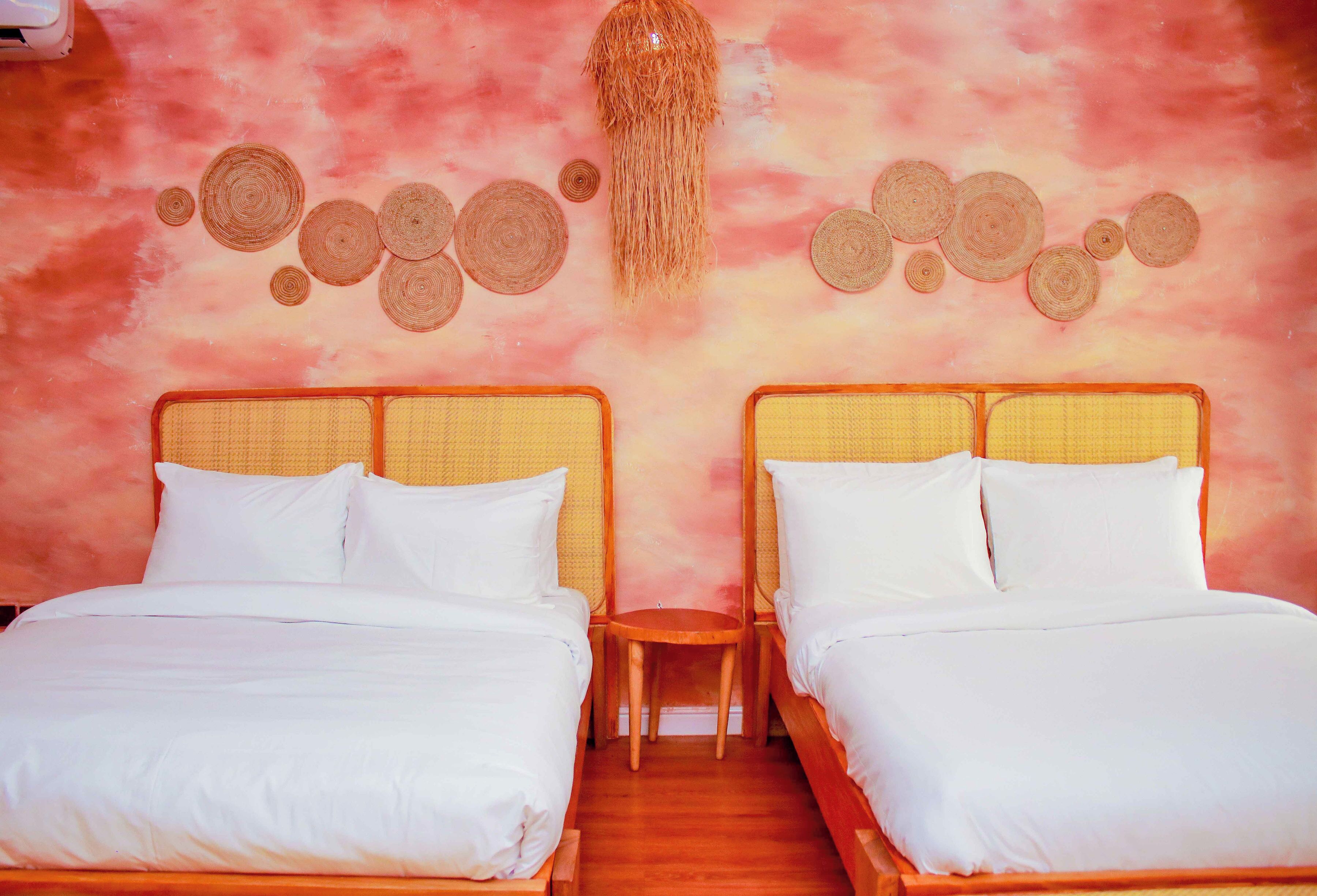 A room with two beds, a small wooden table, and a wall decorated with circular woven patterns.