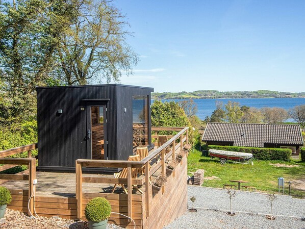 Une terrasse en bois avec une petite structure noire, un banc en bois et une vue sur un lac.
