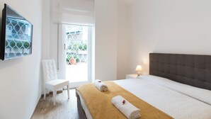 Quarto de hotel com cama, cadeira, mesa de cabeceira com luminária e janela com vista para o exterior.