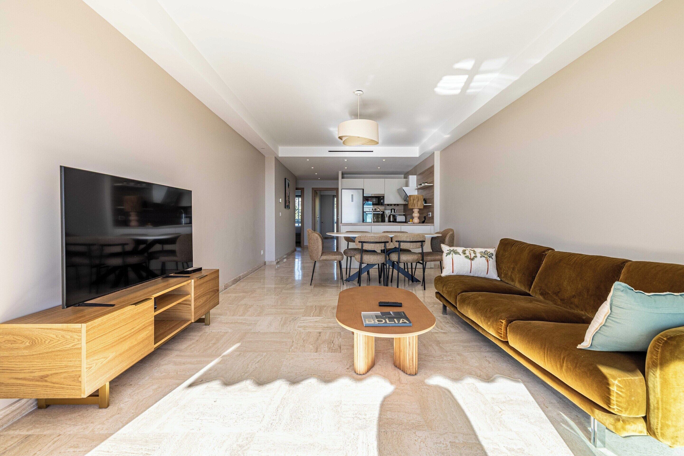 A modern living room with a flat-screen TV, wooden entertainment unit, a brown sofa, and a coffee table.