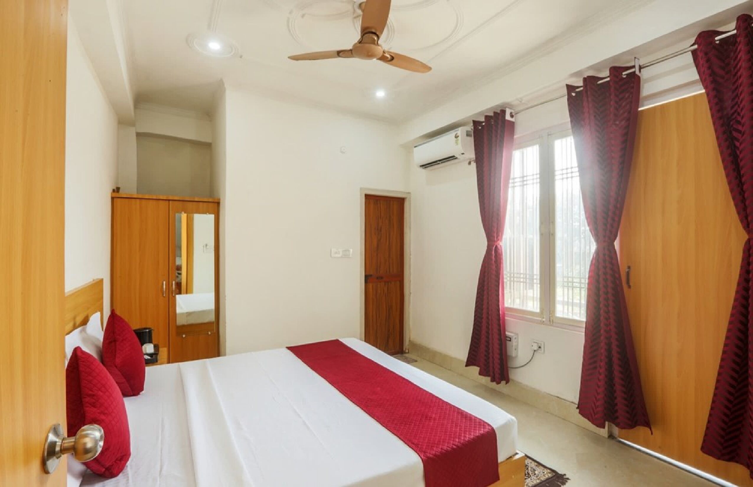 A hotel room with a bed, a ceiling fan, a window with curtains, and a wardrobe.
