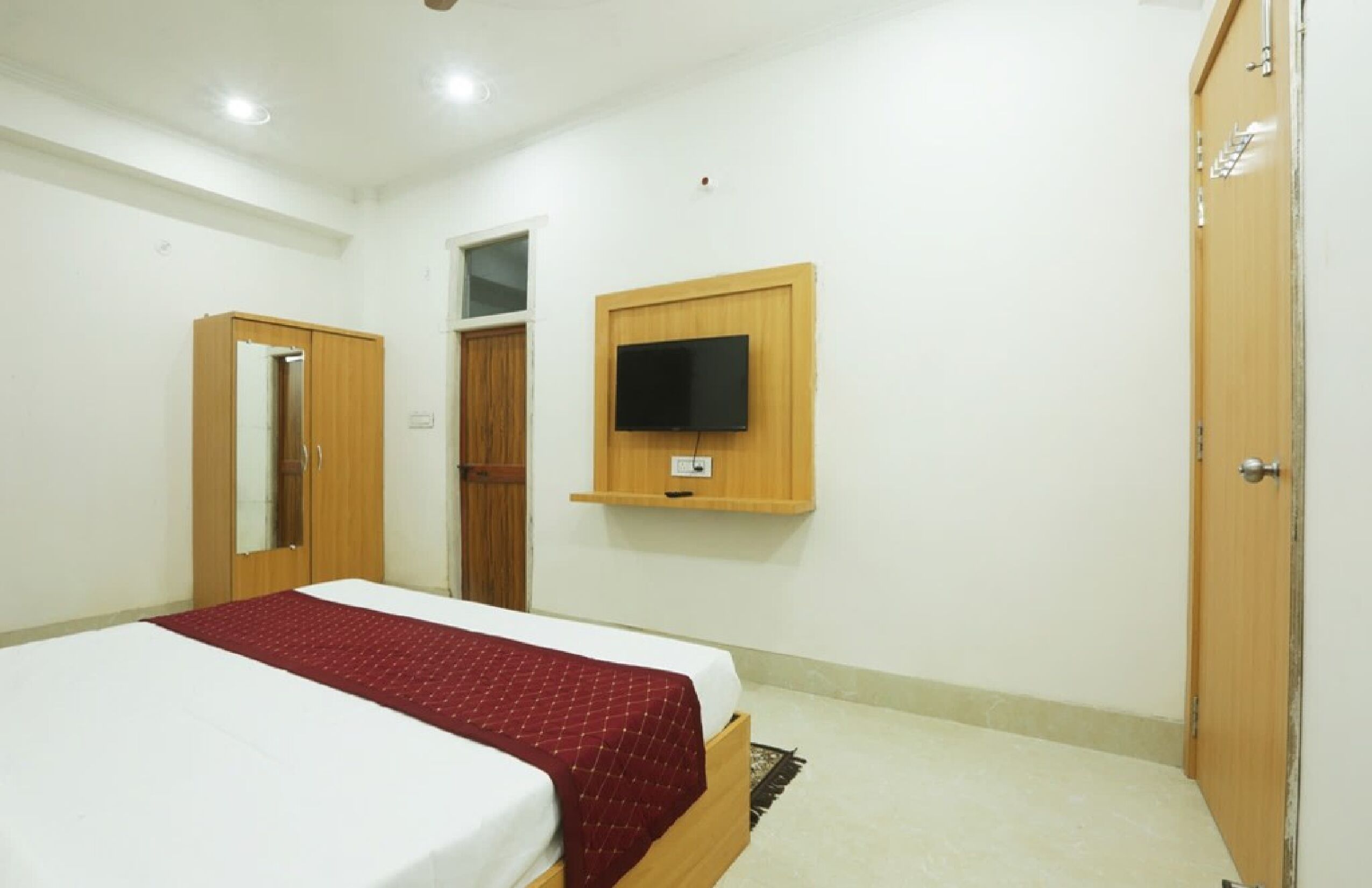 A bedroom with a bed, a wardrobe, a television mounted on the wall, and a door.