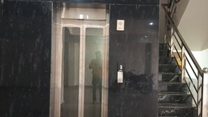 Un ascensor con puerta de vidrio, una escalera con peldaños de mármol negro y un pasamanos.
