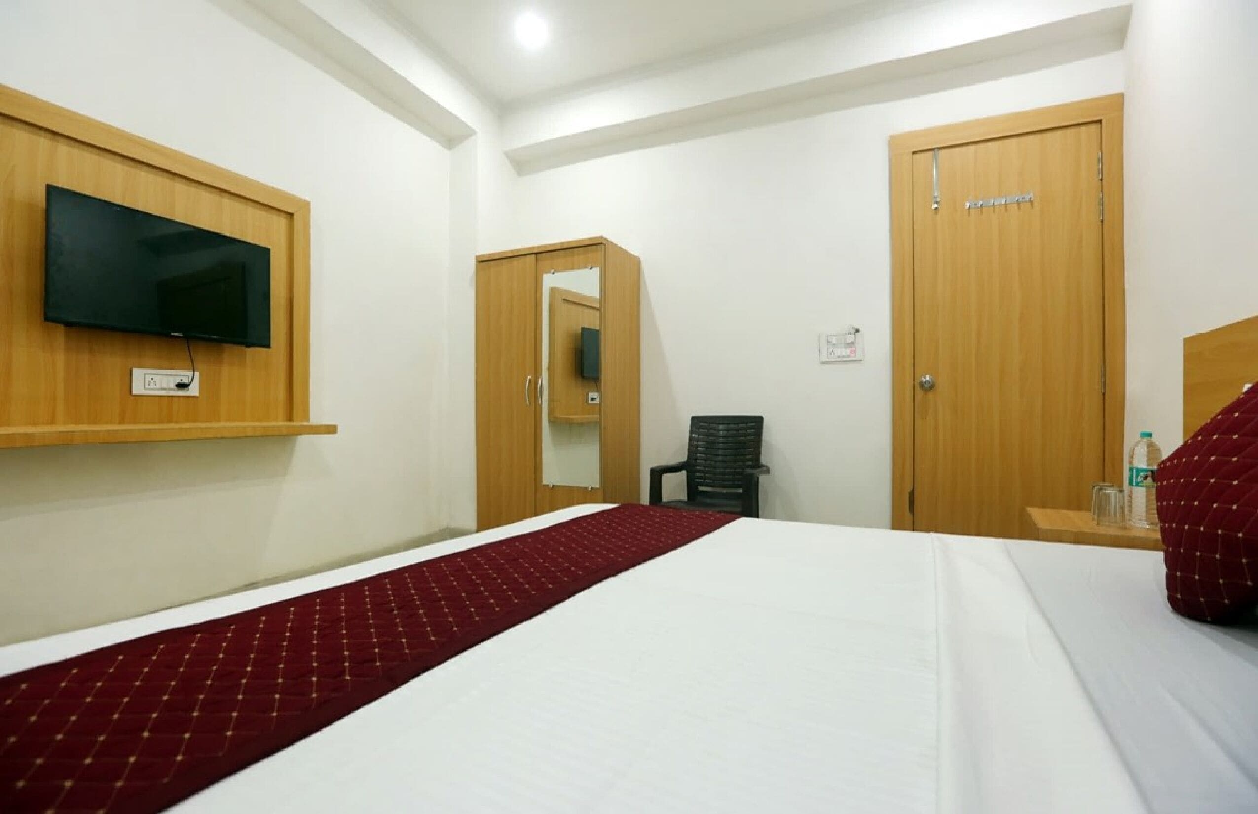 A hotel room with a bed, a TV mounted on the wall, a wardrobe, and a mirror.