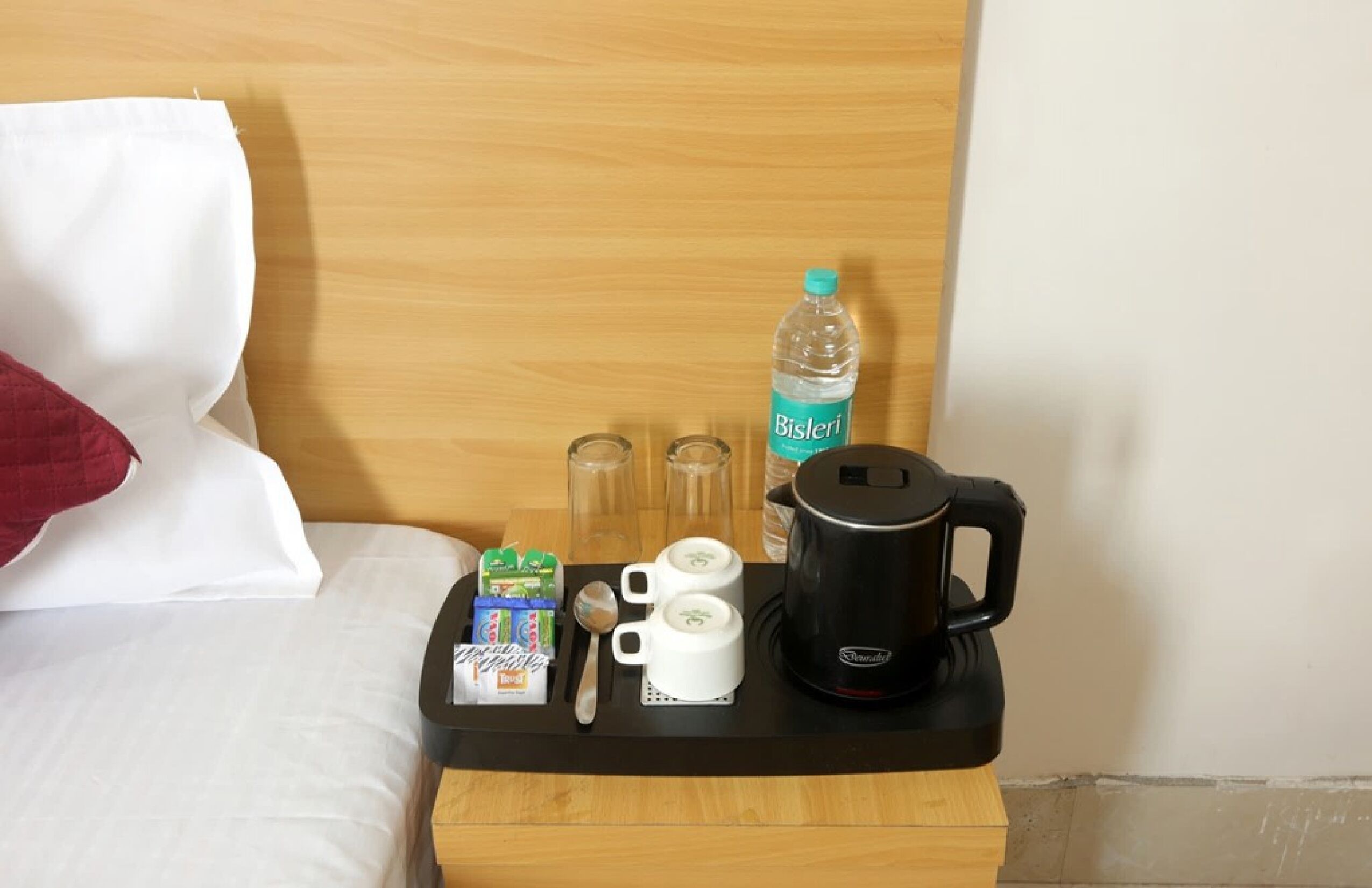 Ett hotellrum med en sänggavel i trä, en säng med vita sängkläder, ett bricka med frukosttillbehör inklusive juice, flingor och en kaffebryggare.