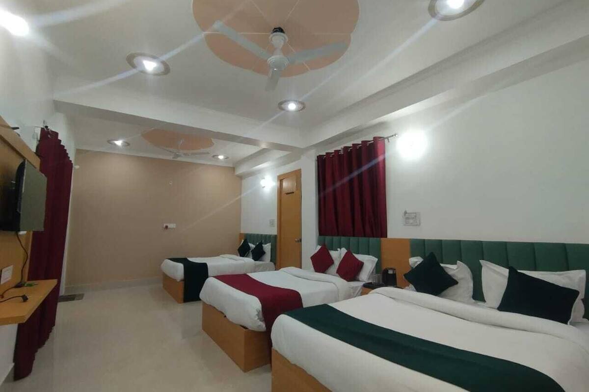 A hotel room with three beds, a ceiling fan, recessed lighting, and a television on a stand.