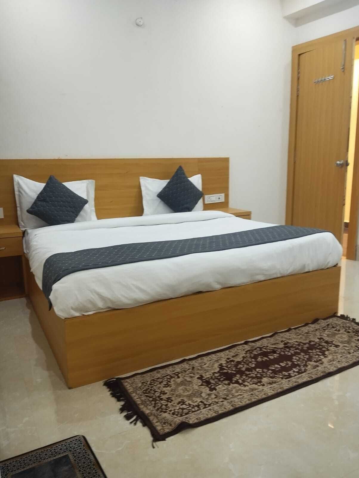 A neatly made bed with a wooden headboard, two pillows, and a dark blanket.