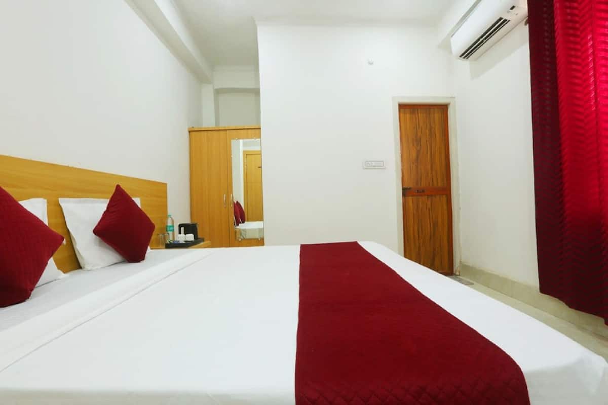 A hotel room with a large bed, a wooden headboard, a red throw blanket, and a red curtain.