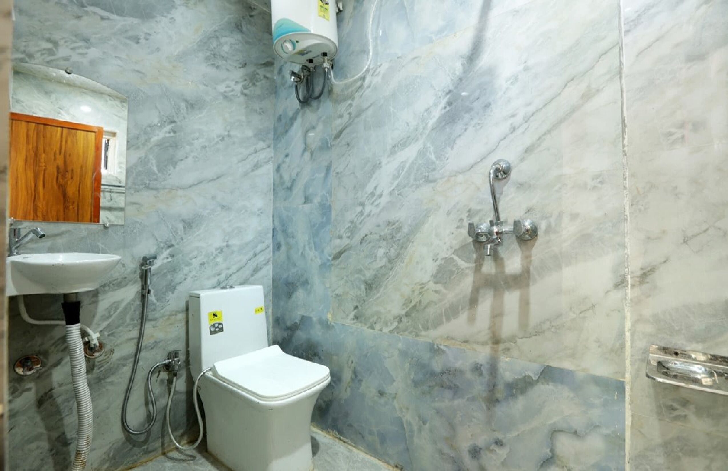 A bathroom with a marble wall, a sink, a toilet, and a shower.