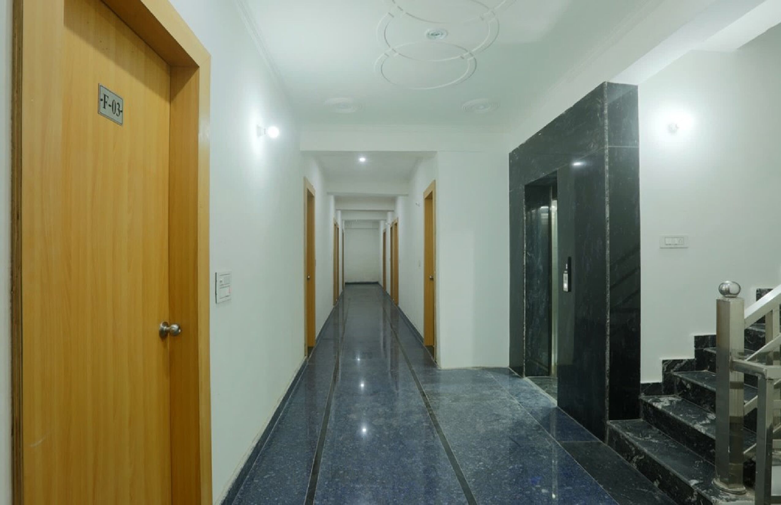 A hallway with wooden doors, a marble staircase, and a long corridor with doors at the end.