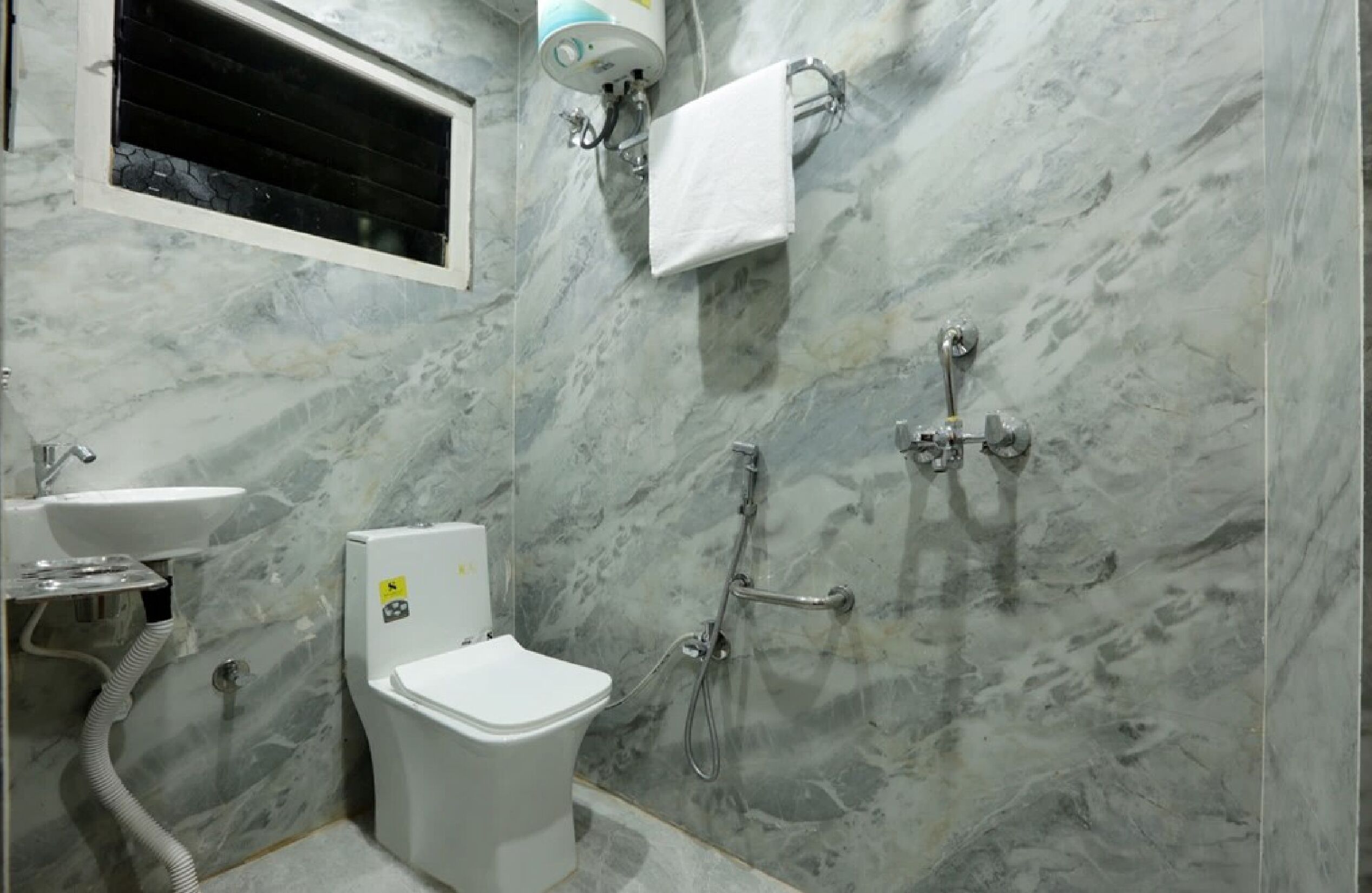 A bathroom with a marble wall, a toilet, a sink, and a shower.
