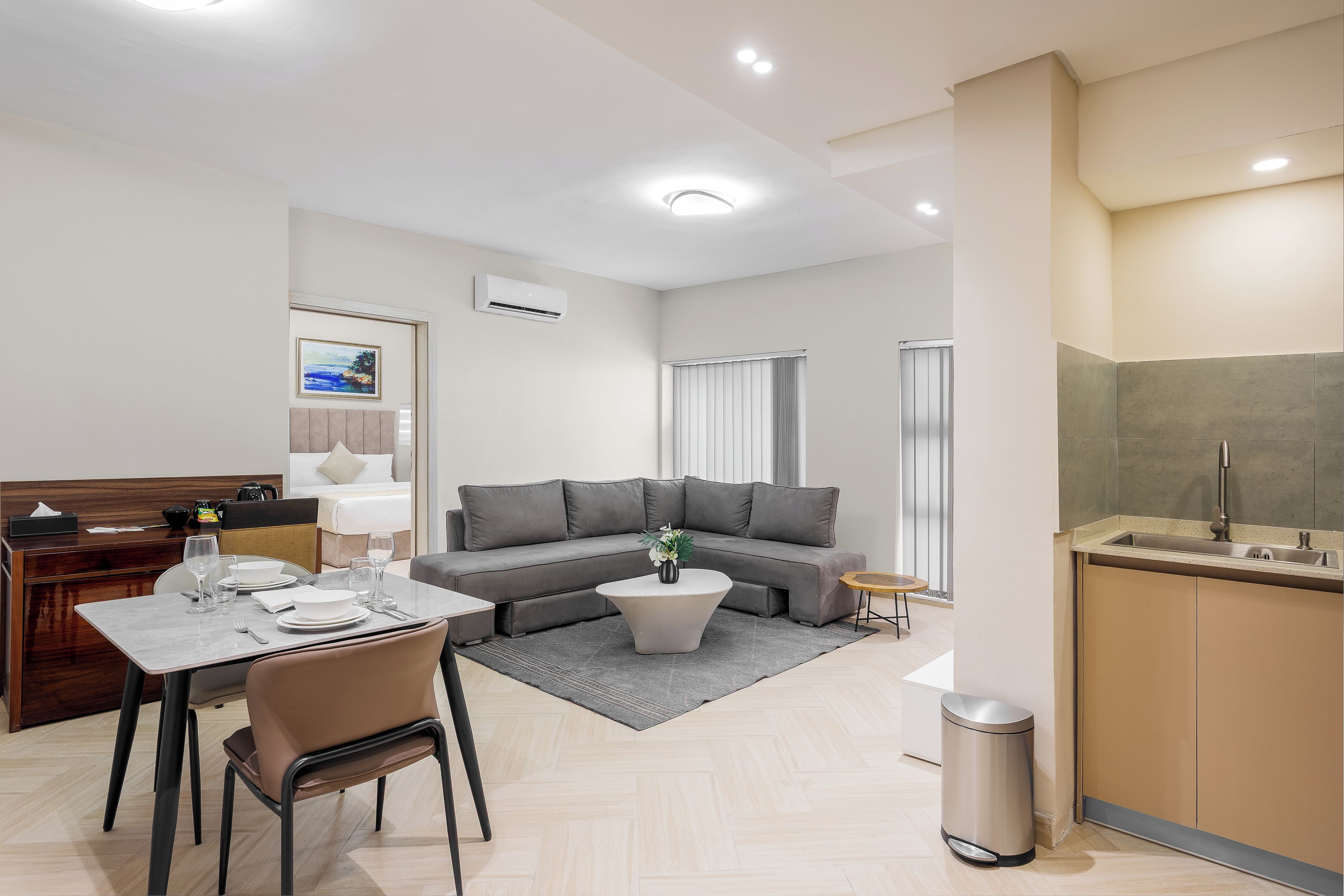 Ein modernes Wohnzimmer mit einem grauen Sofa, einem Esstisch mit Tellern und Gläsern, einem kleinen Couchtisch und einem Mülleimer.